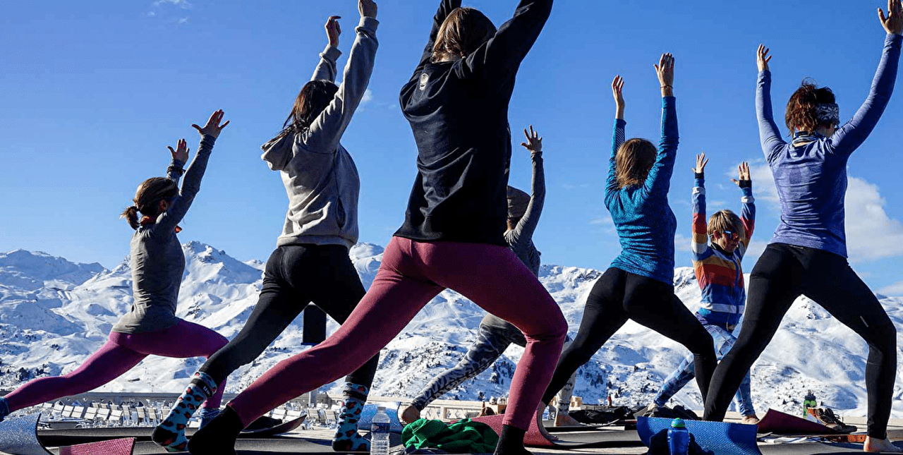 Groupe de personne effectuant des postures de yoga en plein air face à la montagne l'hiver