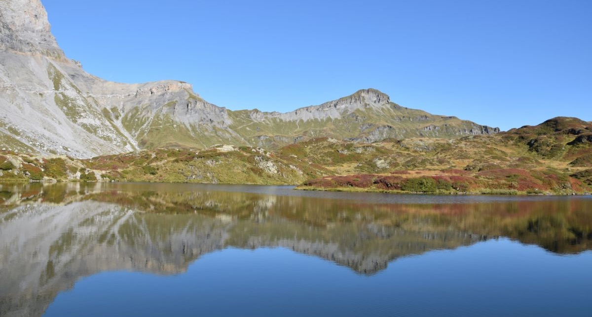 Vue sur un lac de montagne en automne sous un ciel limpide et bleu où pics et sommets se reflètent à la surface