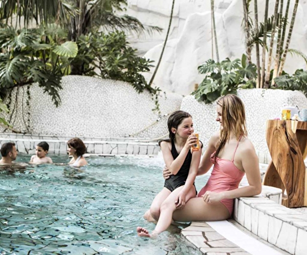 Mère et fille, assises au bord d'une piscine sur les marches sirotant une boisson les pieds dans l'eau