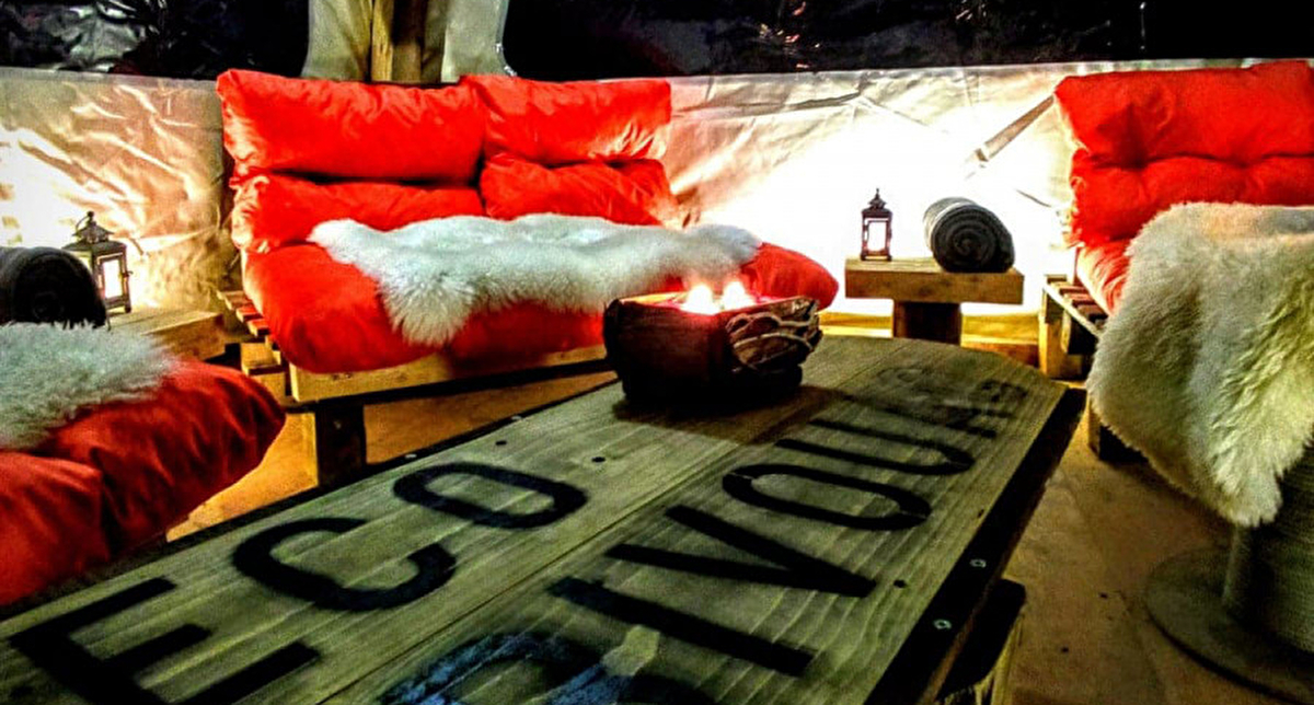 Vue intérieure d'un éco-bivouac et de son espace détente fait de banquettes, coussins et mobilier en bois