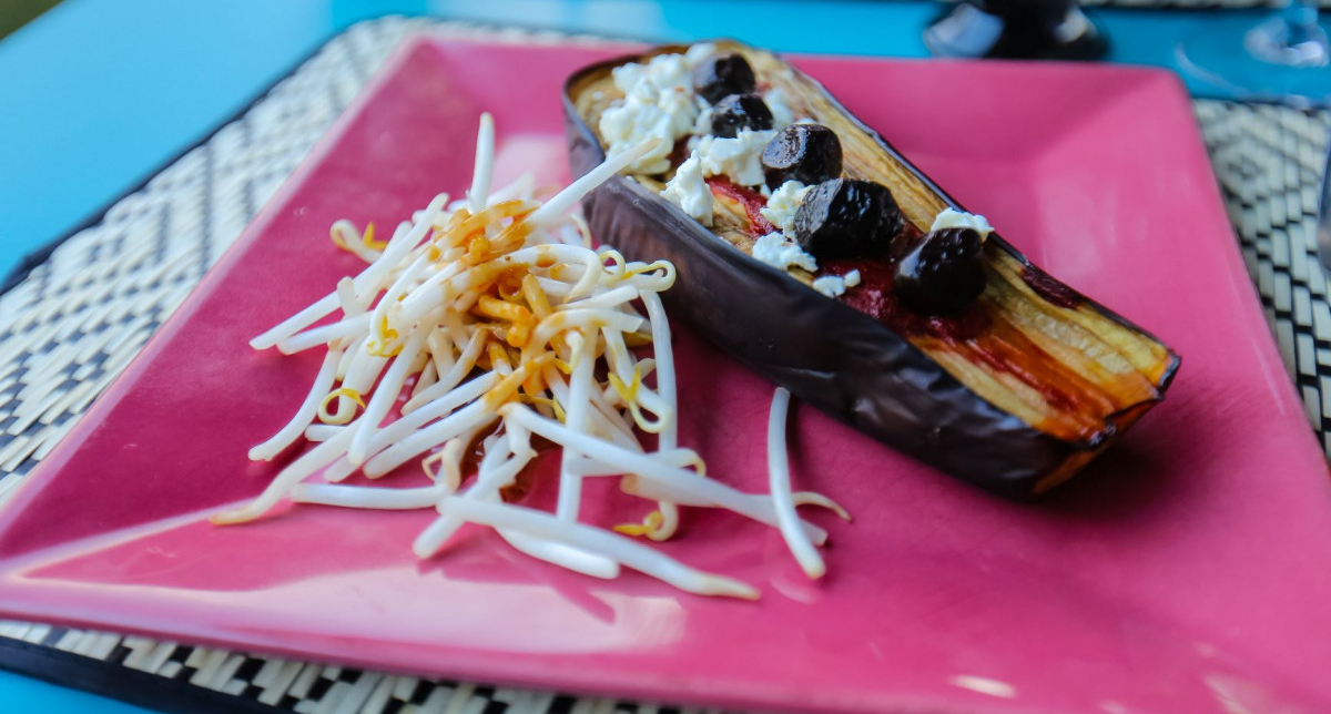 Présentation d'un repas à base d'aubergine, feta et olives dans une assiette rose fushia