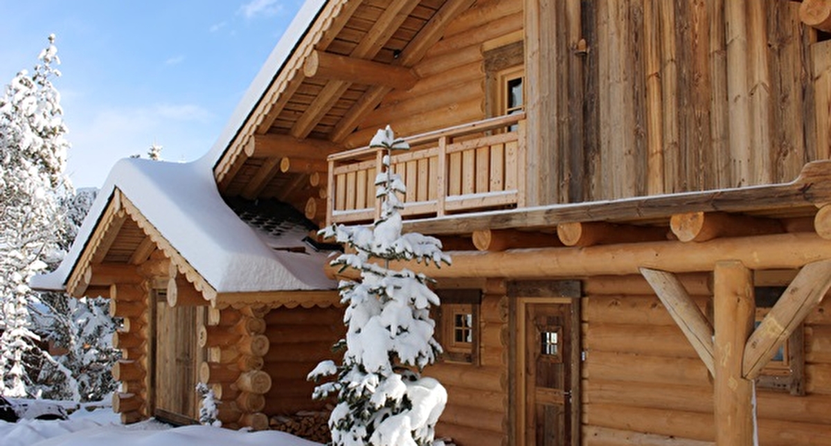 Vue extérieure sur un chalet en bois de grande taille recouvert de neige sous un ciel bleu