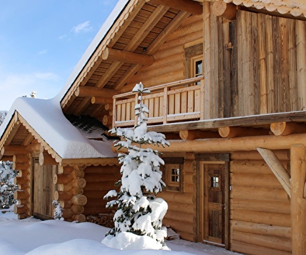 Vue extérieure sur un chalet en bois de grande taille recouvert de neige sous un ciel bleu