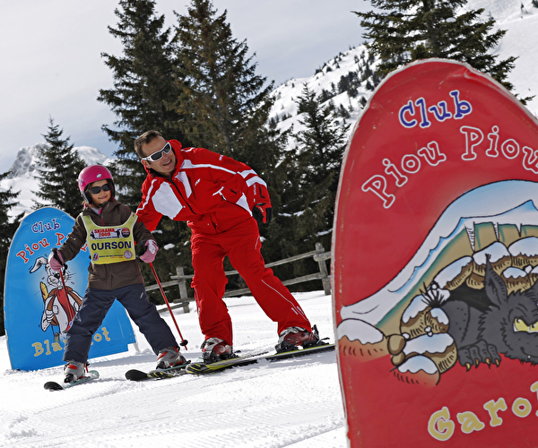 Moniteur de ski aidant une jeune fille à skier et à passer les portes rouge et bleue sur une piste enneigée