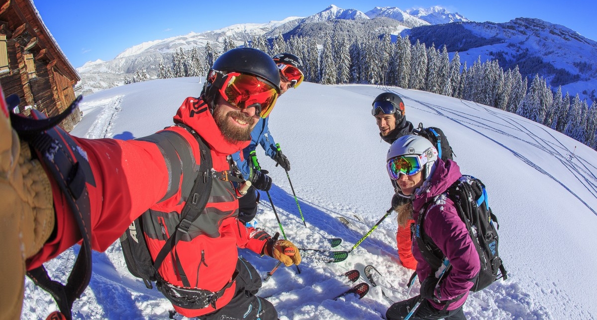 Personnes équipées d'une tenue de ski complète et portant des masques de protection effectuant un selfie devant les montagnes enneigées sur une piste