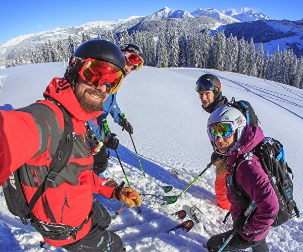 Personnes équipées d'une tenue de ski complète et portant des masques de protection effectuant un selfie devant les montagnes enneigées sur une piste