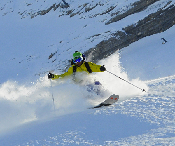 Personne équipée d'une tenue complète pour skier effectuant une descende dans la poudreuse sous le soleil