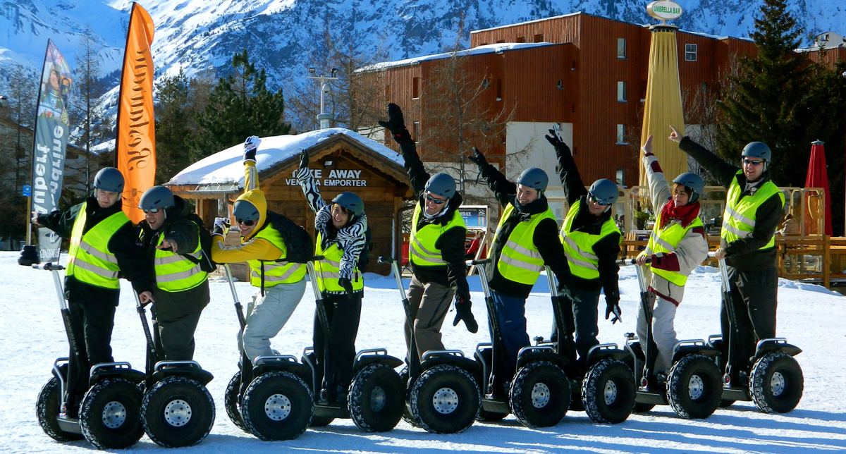 Groupe de personnes équipées de casquest et de gilets jaunes réfléchissants postés sur des Segway en file indienne sur la neige en montagne
