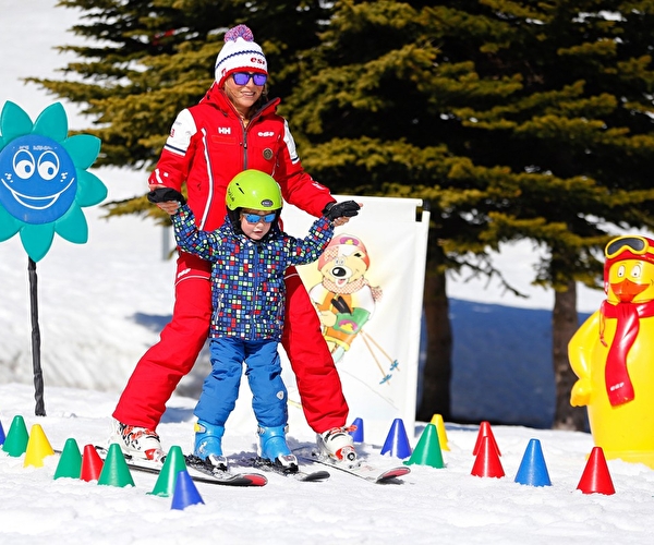 Monitrice de ski ESF apprenant à un enfant à descendre une piste entre des plots de couleurs sur un espace dédié aux jeunes