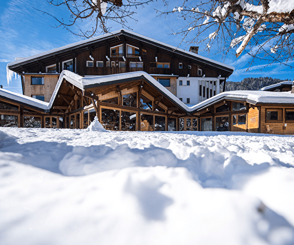 Vue extérieure sur un chalet en bois recouvert de neige permettant l'accueil de personnes