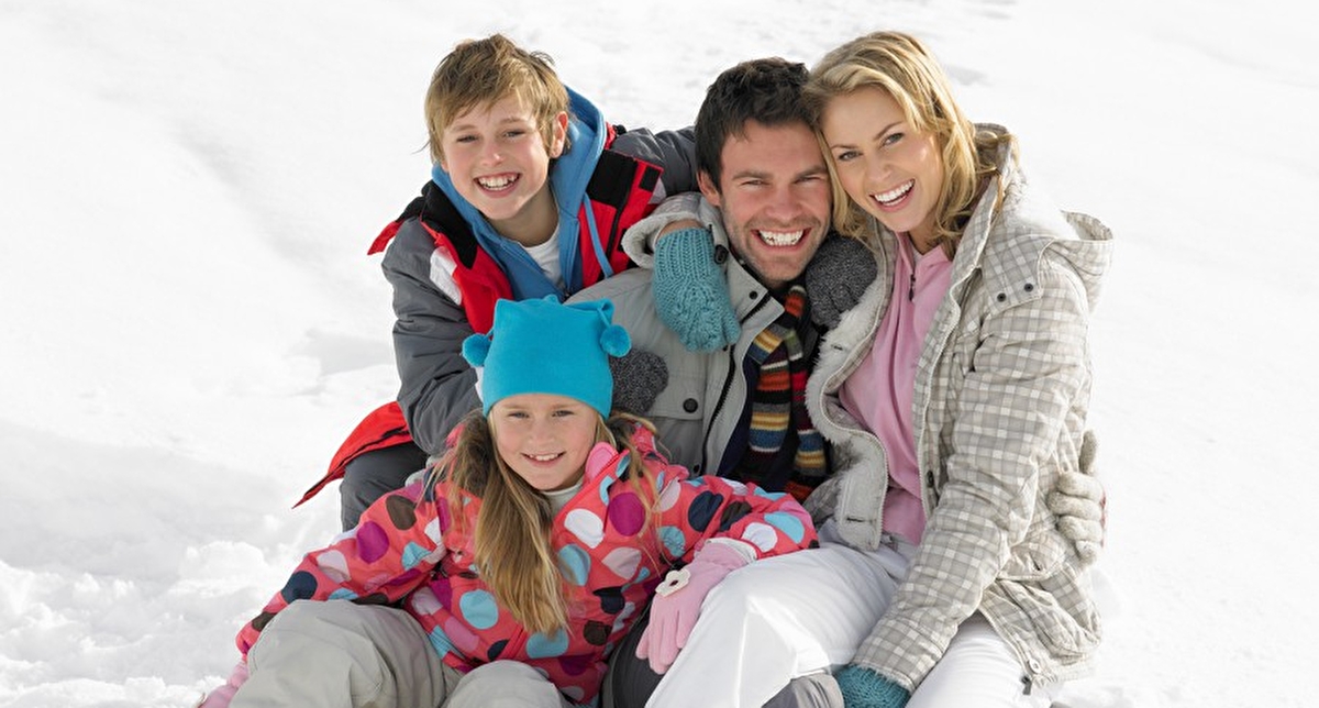 Couple avec enfants assis sur une luge en montagne et équipés de tenues chaudes et de chaussures adaptées à la neige