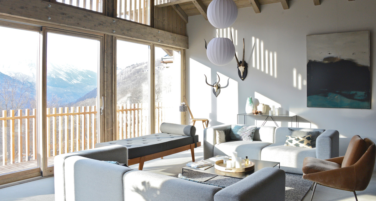Vue intérieure du chalet Home by U avec son salon meublé de canapés et banquette avec vue sur la montagne enneigée