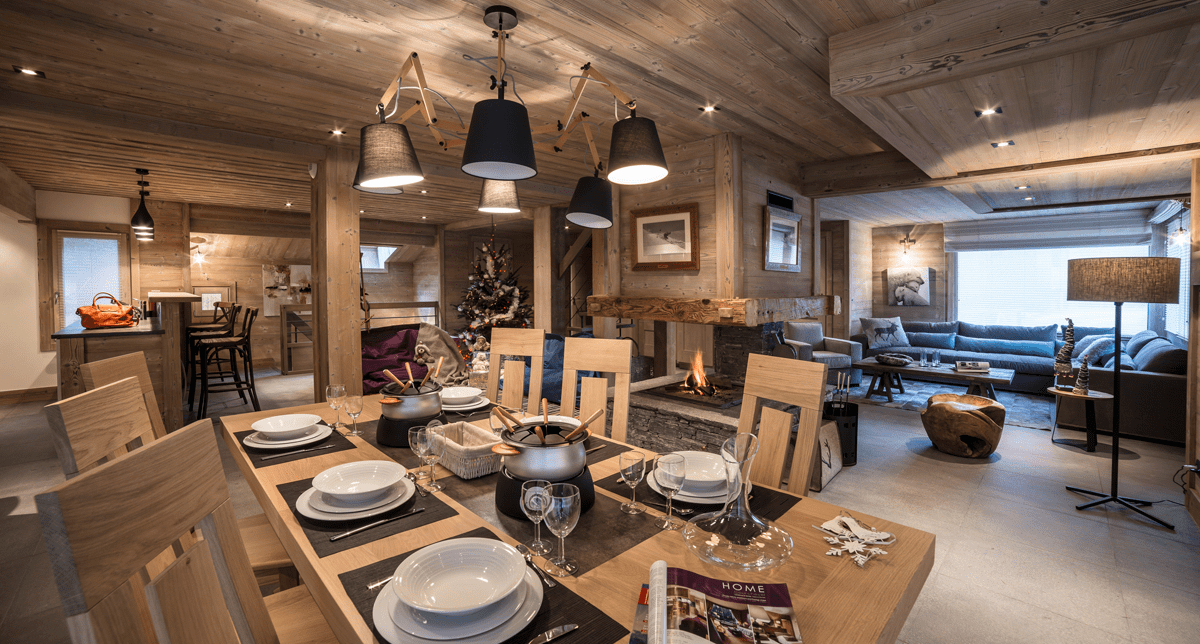 Vue intérieure d'un chalet de montagne contenant plusieurs espaces dédiés au repas et à la détente avec canapés, fauteuils et table à manger