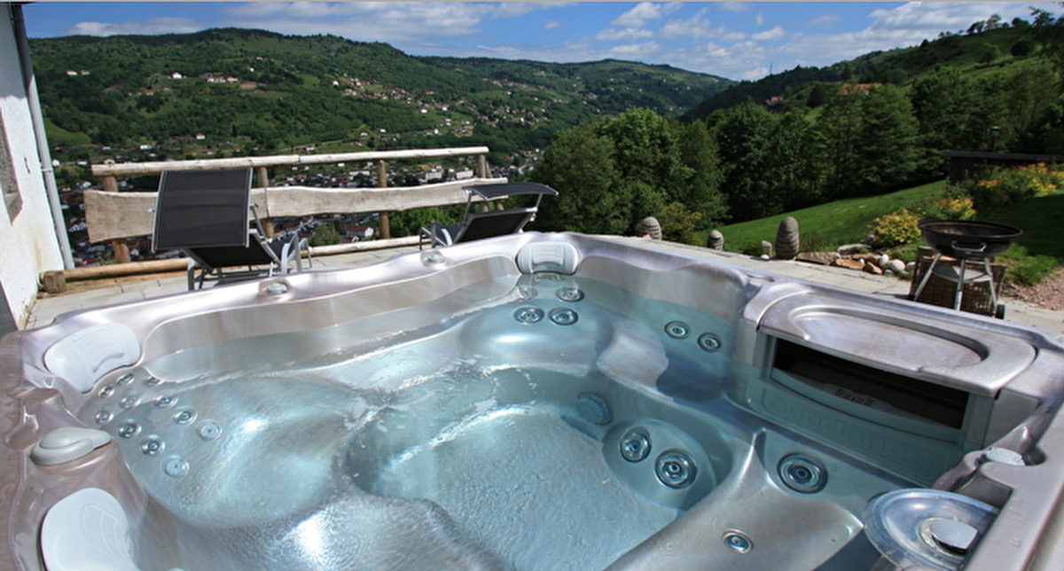 Vue extérieure sur un jacuzzi positionné sur une terrasse bois face au panorama des montagnes vertes