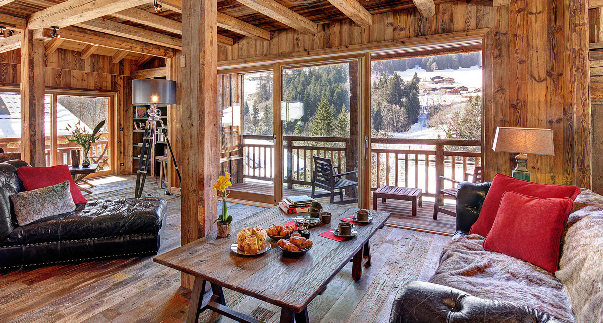 Vue intérieure d'un chalet en bois et de son espace détente et salon avec canapés en cuir et fauteuils avec vue sur les montagnes environnantes