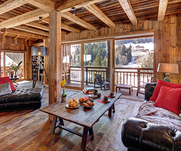 Vue intérieure d'un chalet en bois et de son espace détente et salon avec canapés en cuir et fauteuils avec vue sur les montagnes environnantes
