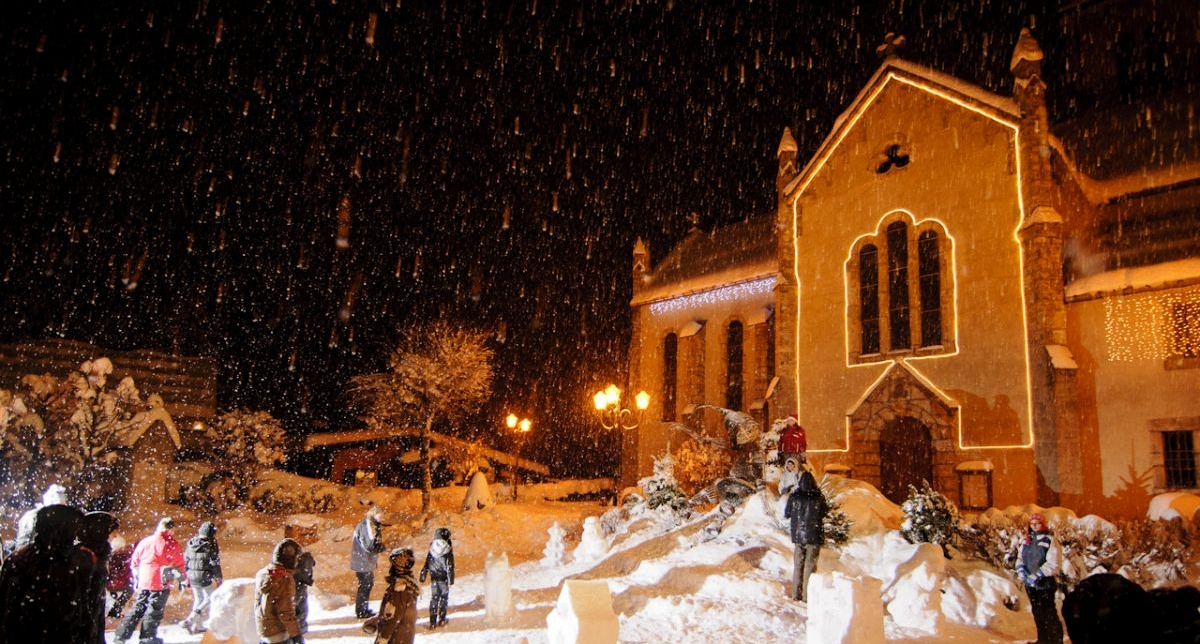 Groupe de personnes se baladant autour de sculptures sur neige près d'une église la nuit