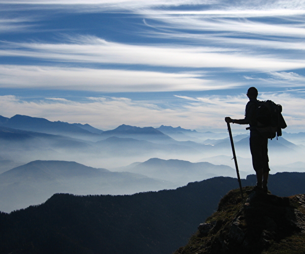 Personne juchée au sommet d'une montagne contemplant la vue des montagnes sous les nuages
