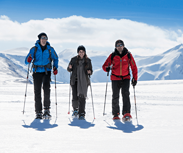 Trio de personnes effectuant une randonnée en raquettes sur la neige face aux sommets des montagnes enneigés