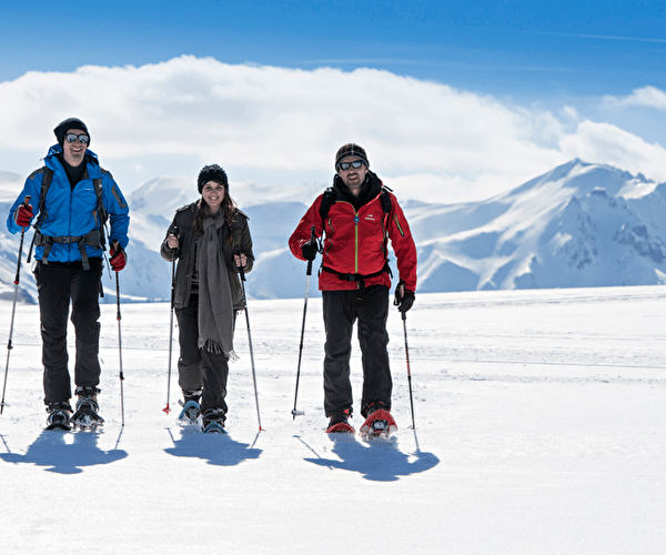 Trio de personnes effectuant une randonnée en raquettes sur la neige face aux sommets des montagnes enneigés