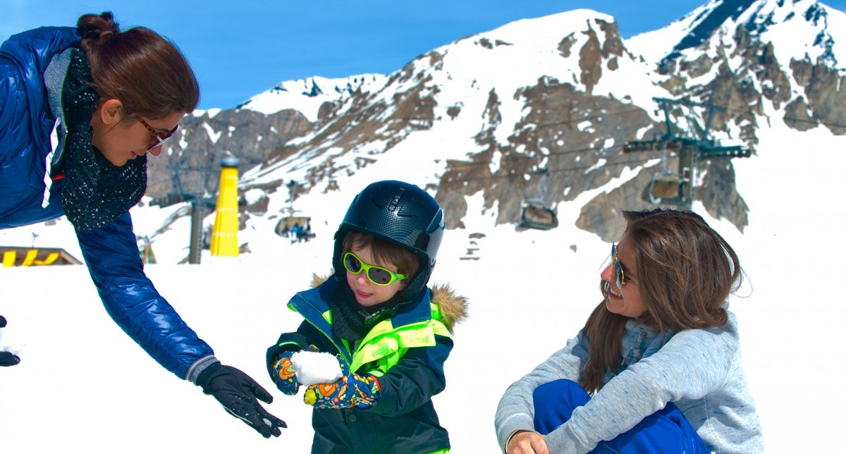 Jeunes femmes s'occupant d'un enfant en l'occupant à faire des boules de neiges face aux montagnes