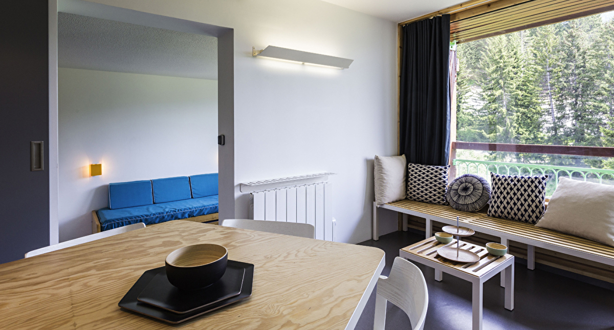Vue intérieure d'un logement de montagne avec espace détente, banquettes et coussins mais aussi une table pour déjeuner