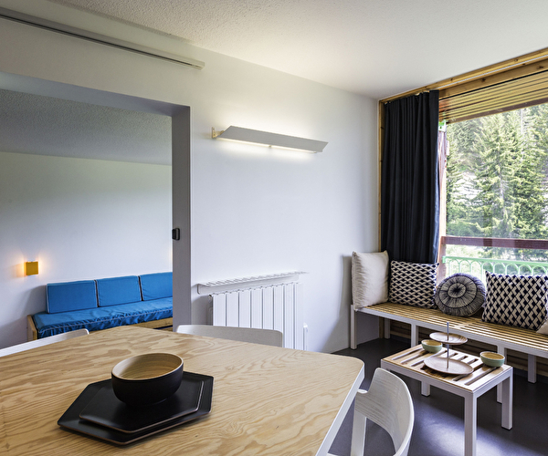 Vue intérieure d'un logement de montagne avec espace détente, banquettes et coussins mais aussi une table pour déjeuner