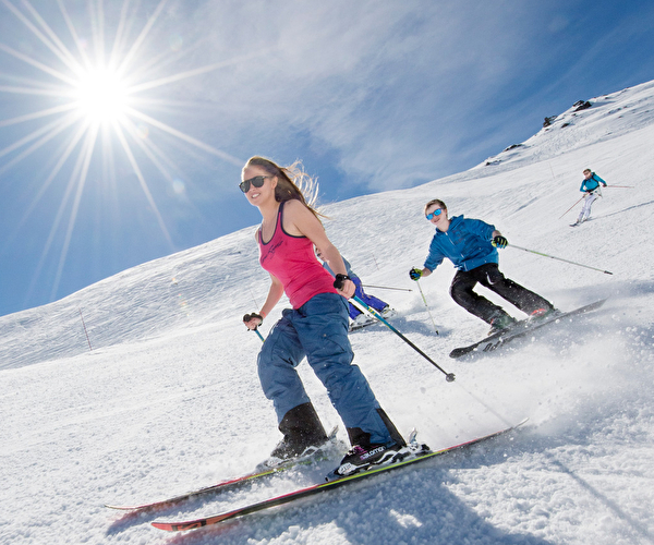 Personnes effectuant une descente à ski sur une piste de montagne sous le soleil
