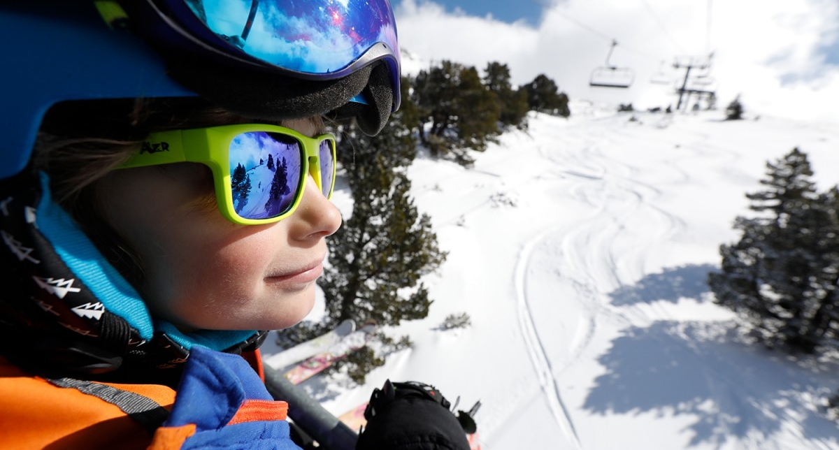 Enfant sur un télésiège portant un casque et des lunettes de soleil et regardant le paysage